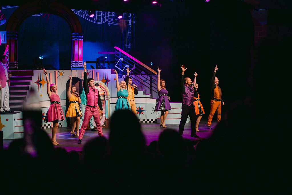 colorful cast in costumes hands up